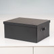 A black storage box with a lid, featuring a handle on the front. It is positioned on a white surface against a light background. A black storage box with a lid, featuring a handle on the front. It is positioned on a white surface against a light background.